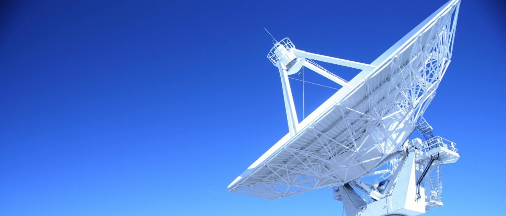 A large satellite dish observatory against a clear blue sky in a desert landscape, capturing signals.